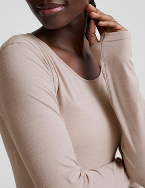 model wearing a beige long-sleeve crewneck top and black pants on a plain background. 