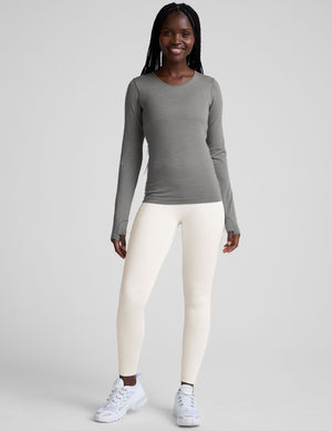 model wearing a gray long-sleeve crewneck top and white pants on a plain background. 
