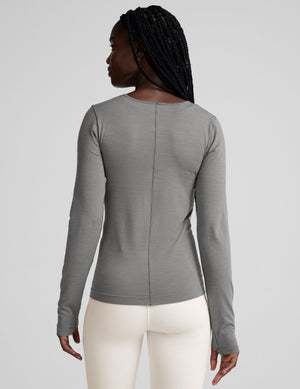 model wearing a gray long-sleeve crewneck top and white pants on a plain background. 
