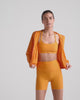 Video of a woman in an orange run jacket and orange bra and biker shorts. 