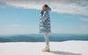 video of a girl in a blue long length puffer jacket, girl in a red set, man and woman jumping off a rock, and lastly a girl in a quilted jacket and matching set. 