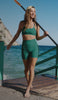 Woman wearing a green bra and biker shorts walking on the beach. 