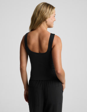 A woman shown from the back wearing a black sleeveless top with a wide scoop neckline and black wide-leg pants, photographed against a light gray studio background.