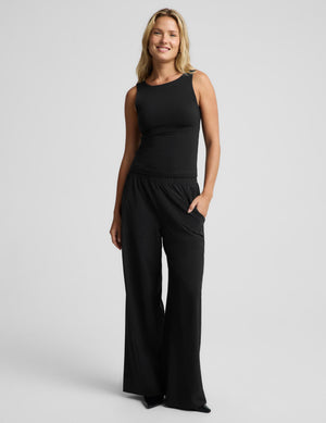 A woman modeling a black sleeveless top and matching wide-leg pants against a light gray studio background.