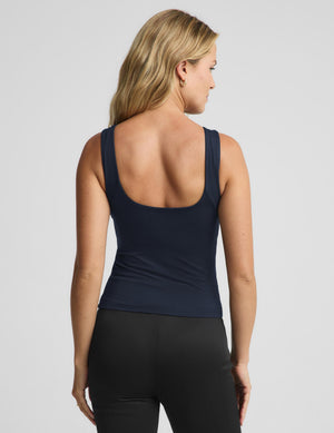 A woman shown from the back wearing a navy blue scoop-neck tank top and black leggings against a light gray studio background.